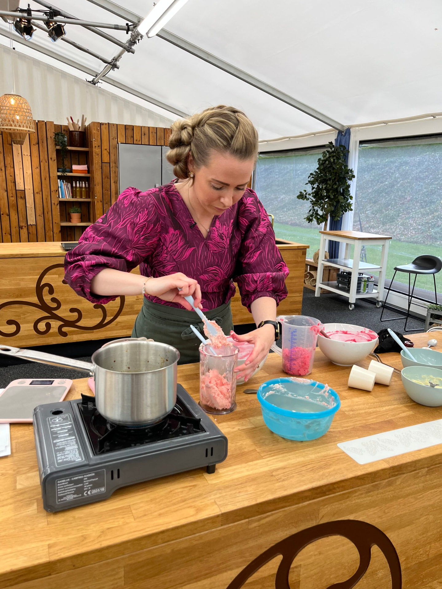 Nicole rører en lyserød marcipanmasse i et målebæger ved komfuret under et kursus i bageteltet
