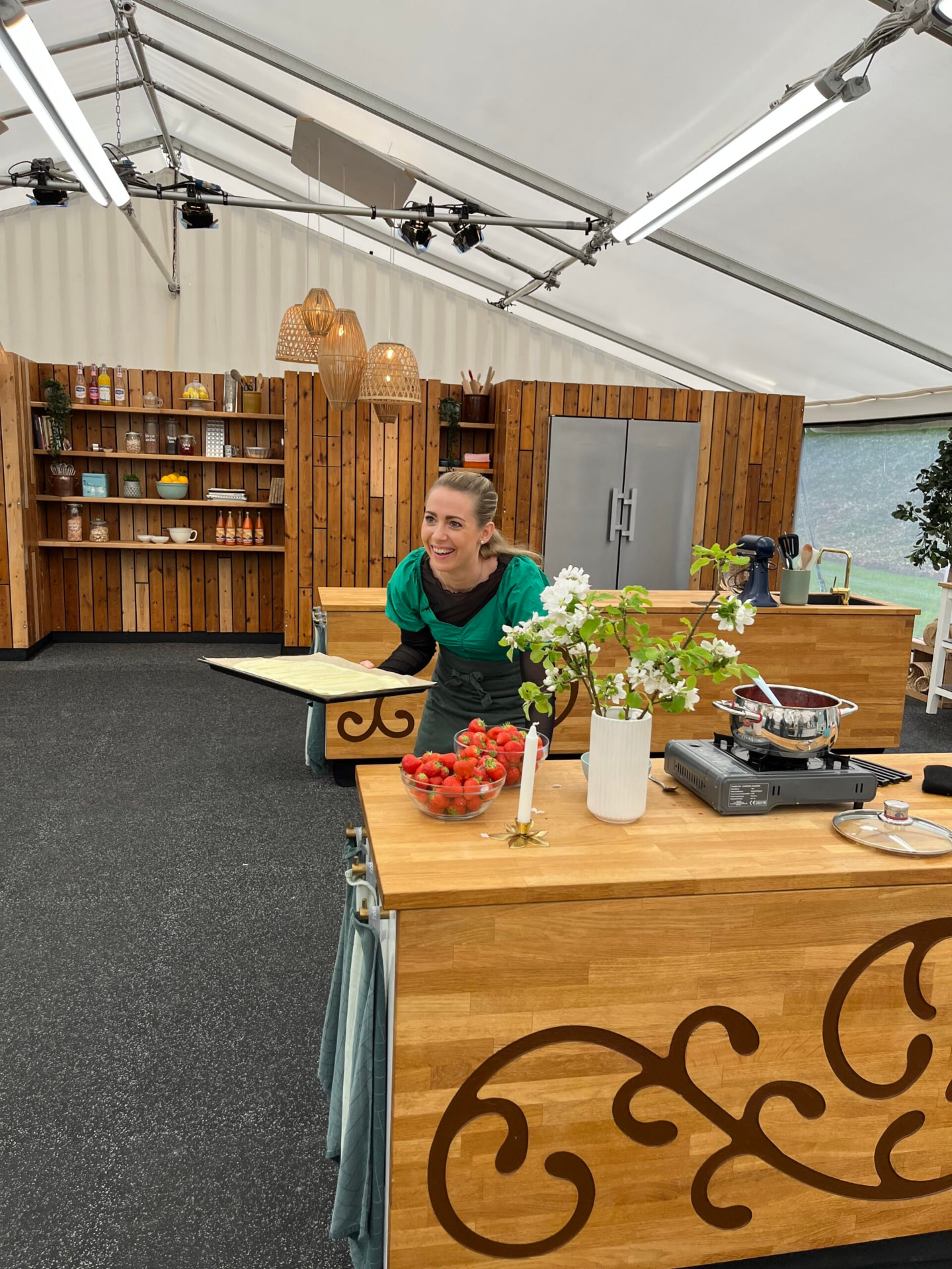 Nicole griner med en bageplade i hånden i det store bagetelt med jordbær på bordet